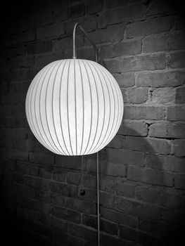 Lamp with round lampshade on brick wall. Image in black and white tones, with vignette.