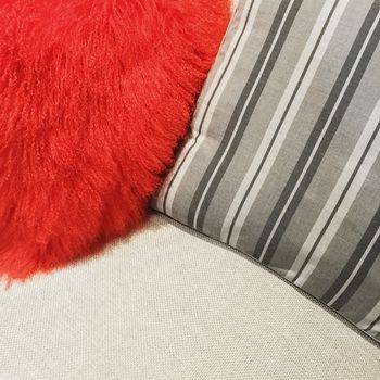 Close-up of cushions decorating a sofa. Red dyed sheepskin and striped gray material.