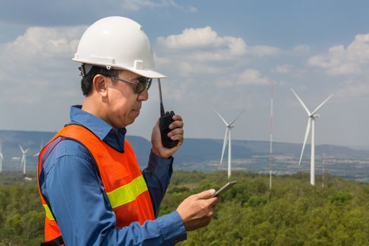 Male Architect or Engineer, use Hand-Held Transceiver Radio and Digital Wireless Tablet Device, working at Wind Turbine Power Generator Field as Infrastructure Construction Project Development