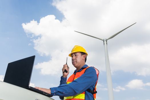 Architect or Engineer use Laptop computer and Transceiver handheld Radio to Communicate with Headquarter or Center working under Wind Turbine Power Generator as Project Development Equipment concept.