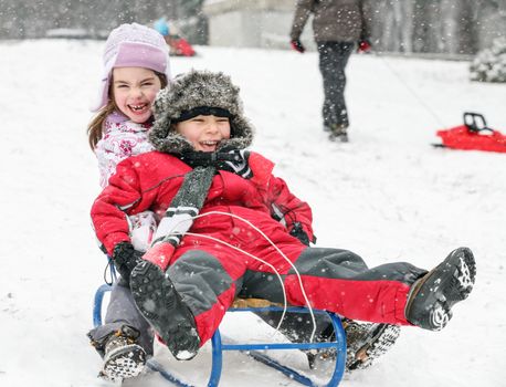 Couple kids, a boy and a girl are sledding in a cold winter day