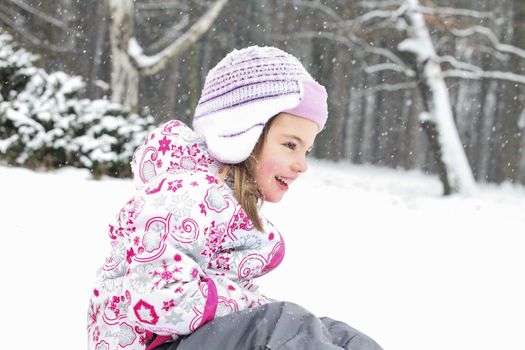 Happy smiling girl is playing on the snow in a cold winter day.