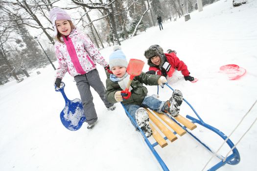 Three kids are playing with sleds in a cold winter day in the park.