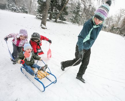 Mother is playing with kids in the snow with sled in cold winter day.