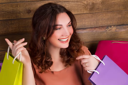 Woman after shopping with colourful paper bags with wooden wall on background