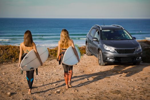 Two beautiful surfer girls near the coastline with her car, and getting ready for surfing