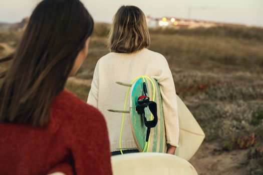 Two female surfers walking near the coastline with surfboards