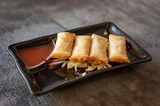 Fried spring rolls on black iron plate on grey stone slate background. side view,close up.