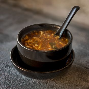 Sour soup on black iron plate on grey stone slate background. side view,close up.