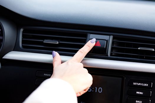 Closeup shot of woman's manicured finger pressing the emergency button on a car's dashboard