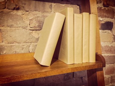 Books on a wooden shelf near a brick wall. Retro style photo.