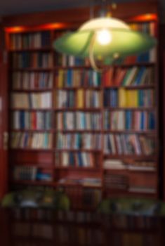 Defocused image of a bookcase and a green lamp. Detail of a living room or a library. Can be used as background.