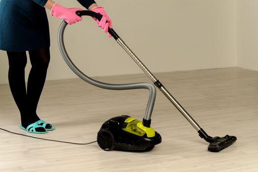woman in pink gloves cleans the floor with vacuum cleaner