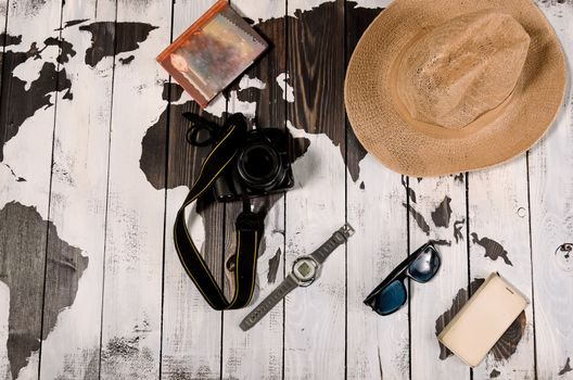 Table with open map showing plans for travelling and related items including watch smartphone sunglasses hat notebook and camera on wooden background with copyspace left