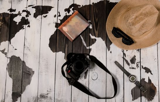 Table with open map showing plans for travelling and related items including watch sunglasses hat notebook and camera on wooden background with copyspace left.