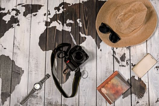 Table with open map showing plans for travelling and related items including watch smartphone sunglasses hat notebook and camera on wooden background with copyspace top left.