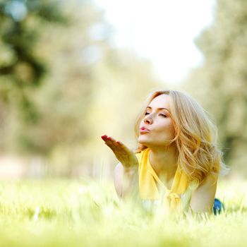 Young woman blows a kiss lying on green grass meadow