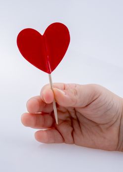 Little red color heart shape at the top of a stick in hand