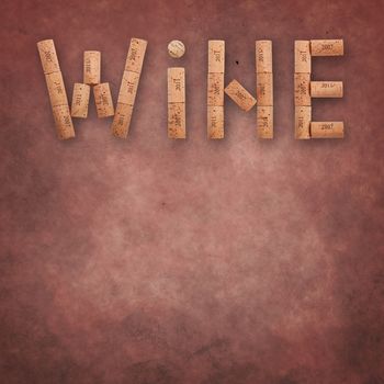 Word WINE shaped by natural wooden wine bottle corks of different vintage years over abstract grunge brown pink background