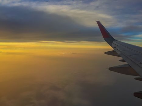 High altitude in flight passenger jet airliner airplane wing, with a cloudy sunset colourful sky.