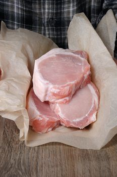 A pile of fresh chopped raw pork steaks over the bones in wrapping paper in the hands of a man