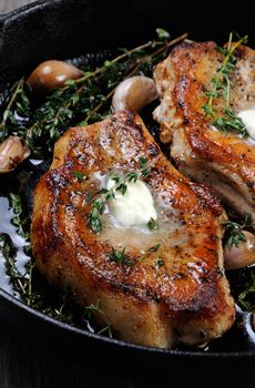 Juicy, browned pork steak on a bone in oil with garlic and herbs in a frying pan. 