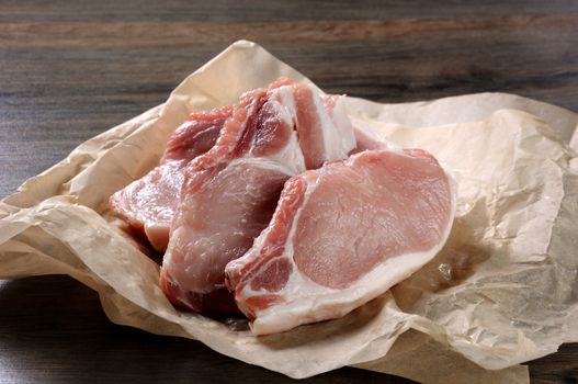 A pile of fresh chopped raw pork steaks over the bones in the wrapping paper on the table. Close-up.
