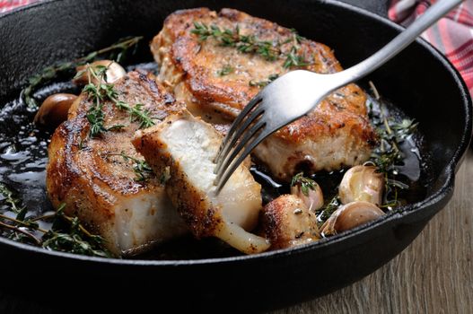 A slice of pork steak cut from fried in oil with garlic and herbs a piece in a frying pan. Close-up.