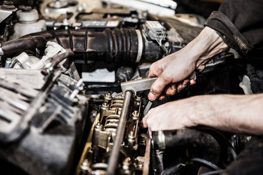 Automobile service worker or garage mechanic hand holding vehicle motor maintenance tool repairing auto car engine