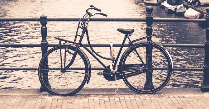 Old bicycle locked on a bridge over water canal, Amsterdam, Netherlands.