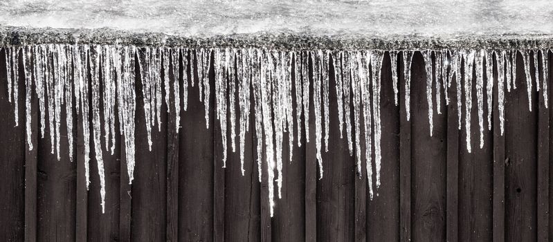 Row of icicles hanging on the roof. Rural winter scene.
