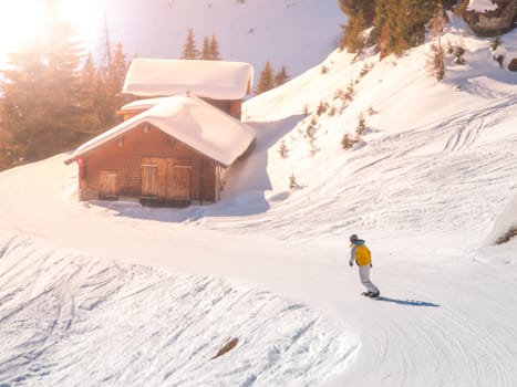 Snowboardist on a ski slope at alpine hut on sunny day, Alps.