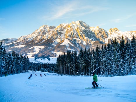 People on ski slope in mountain resort on sunny winter morning.