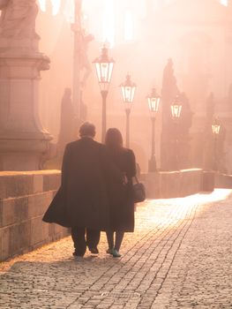 Man and woman couple walk on Charles Bridge in foggy morning, Prague, Czech Republic. Romantic Prague theme.