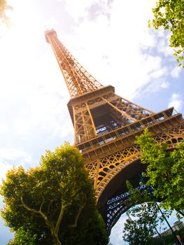 Bottom view of Eiffel Tower on sunny summer day, Paris, France. Sun leak effect.