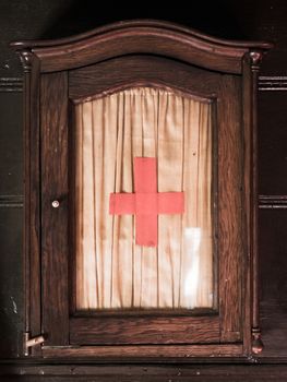 Vintage wooden first aid kit cabinet with glass door and red cross sign.