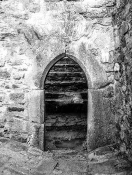 Old gothic arc gate in medieval stone castle ruin. Black and white image.