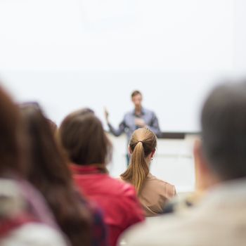 Male speaker giving presentation in lecture hall at university workshop. Audience in conference hall. Rear view of unrecognized participant in audience. Scientific conference event.