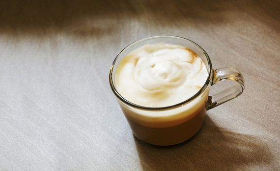 Glass mug with foamy cappuccino on a rough marbled floor . Interior shot