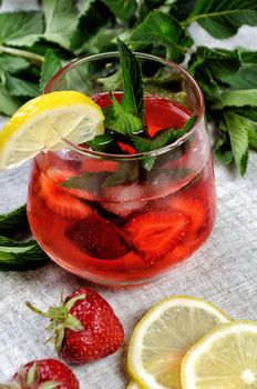 A glass of chilled strawberry lemonade, mint leaves, a slice of lemon with ice