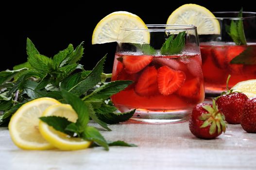 A glass of chilled strawberry lemonade, mint leaves, a slice of lemon with ice