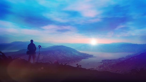 A solitary photographer shoots a fantastic sunrise on a camera in the mountains above the bay. A beautiful landscape is good for tourist and media topics.