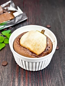 Cake with chocolate and pear in a white bowl, mint on the background of dark wood planks