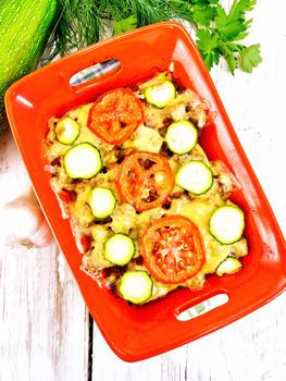 Casserole from minced meat, tomatoes and zucchini in a brazier against a light wooden board on top