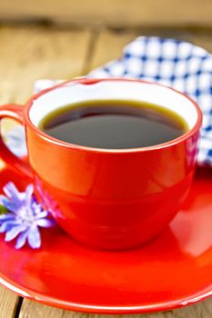 Drink of chicory in a red cup with a flower on a saucer, napkin on a wooden plank background