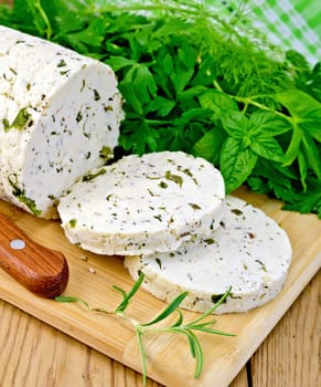 Homemade cheese with herbs and spices, cut into slices, knife, parsley, rosemary and basil, napkin on a background of wooden boards