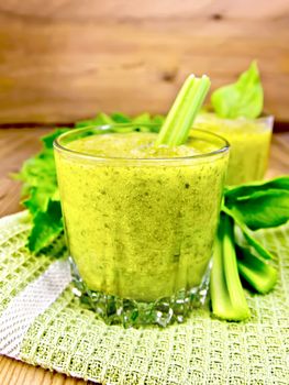 Two glass glassful with a cocktail of celery and spinach on a napkin, stems and leaves against a wooden plank background