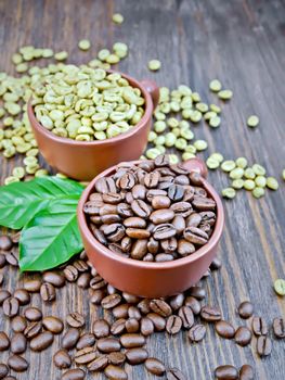 Grains of green and black coffee in brown clay cups and on a table with leaves on a background of a dark wooden board