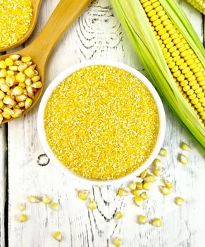 Corn grits in a bowl and spoon, cobs and grains on the background of the wooden planks on top