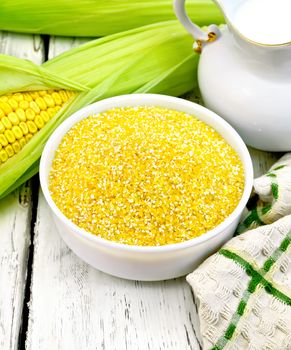 Corn grits in a bowl, cobs, a jug of milk and a napkin on a wooden boards background